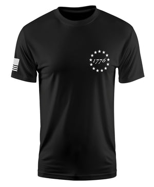 A black short-sleeve crewneck t-shirt featuring a white circular star design with '1776' text on the left chest and a distressed American flag graphic on the right sleeve, shown against a plain white background.