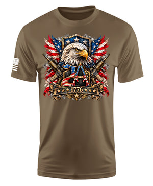 A brown short-sleeve t-shirt with a detailed patriotic graphic on the chest featuring an eagle, crossed rifles, American flags, and the year 1776. A small white American flag is printed on the right sleeve.