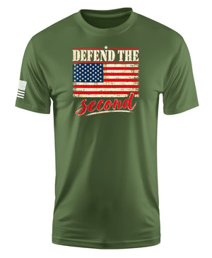 An olive green short-sleeve t-shirt with a distressed graphic on the chest reading 'DEFEND THE second' in beige and red, featuring a US flag. A small black-and-white flag graphic is visible on the right sleeve.