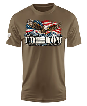A brown short-sleeve crewneck t-shirt featuring a graphic of a bald eagle flying over a mountain range and American flag, with the word 'FREEDOM' printed below. A small black and white American flag is printed on the left sleeve.