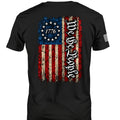 Black short-sleeve t-shirt with a distressed American flag graphic on the back, featuring 'We the People' in gothic lettering and '1776' in a star circle.