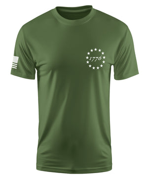 An olive green short-sleeve crewneck t-shirt with a white circular star design and '1776' text on the left chest, and a black-and-white American flag graphic on the right sleeve, shown on a plain white background.