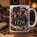 A white ceramic mug with a detailed 1776 American Revolutionary themed graphic print, displayed on a rustic wooden table surrounded by historical and military props.