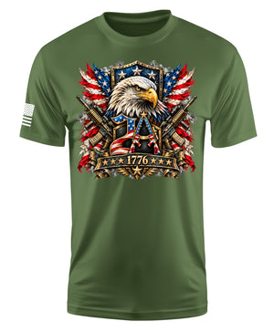 An olive green short-sleeve t-shirt with a large patriotic graphic on the chest featuring an eagle, crossed rifles, American flags, and the year 1776. A small black-and-white American flag is printed on the right sleeve.
