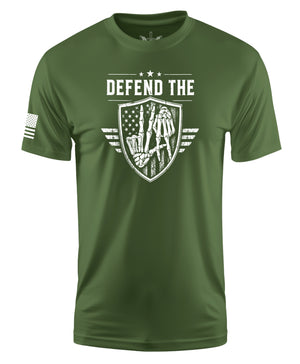 An olive green short-sleeve t-shirt with a distressed white graphic on the chest reading 'DEFEND THE' above a shield design featuring a soldier and an American flag. A small white American flag graphic is printed on the right sleeve.