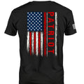 A black short-sleeve t-shirt shown from the back, featuring a distressed vertical American flag graphic with the word 'PATRIOT' printed in red down the right side of the flag. A small white graphic is visible on the left sleeve.